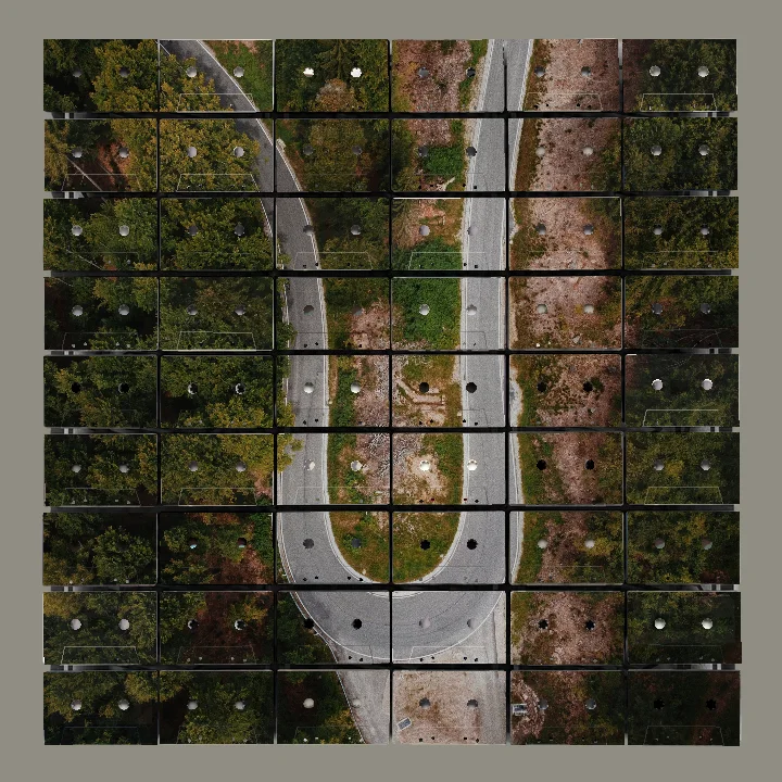 Aerial view of a U-shaped road bend surrounded by dense green trees and patches of brown earth.
