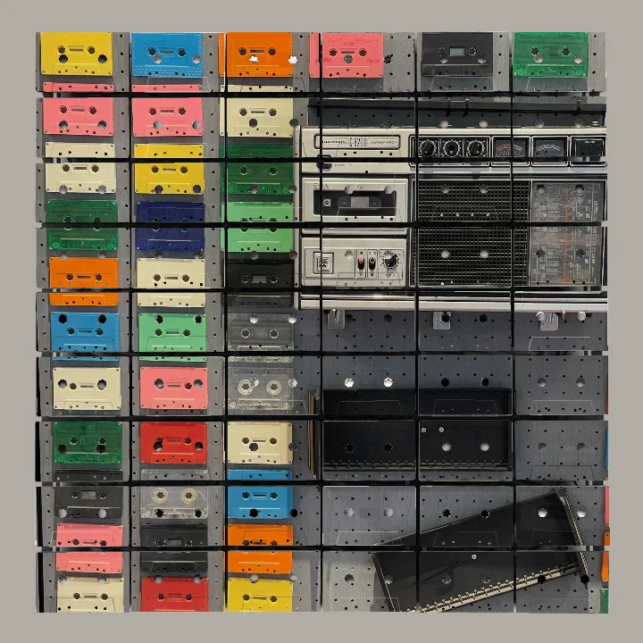 Several rows of colorful cassette tapes mounted on a gray pegboard with a vintage silver radio and two black cassette holders attached.
